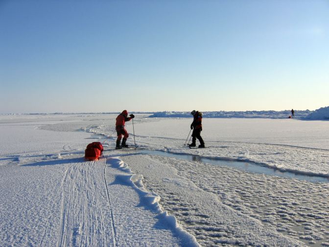 Two men cross an open water lead with the lead sled first