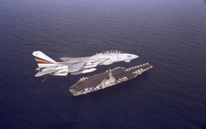 This f14 tomcat flys above the aircraft carrier, uss kitty hawk